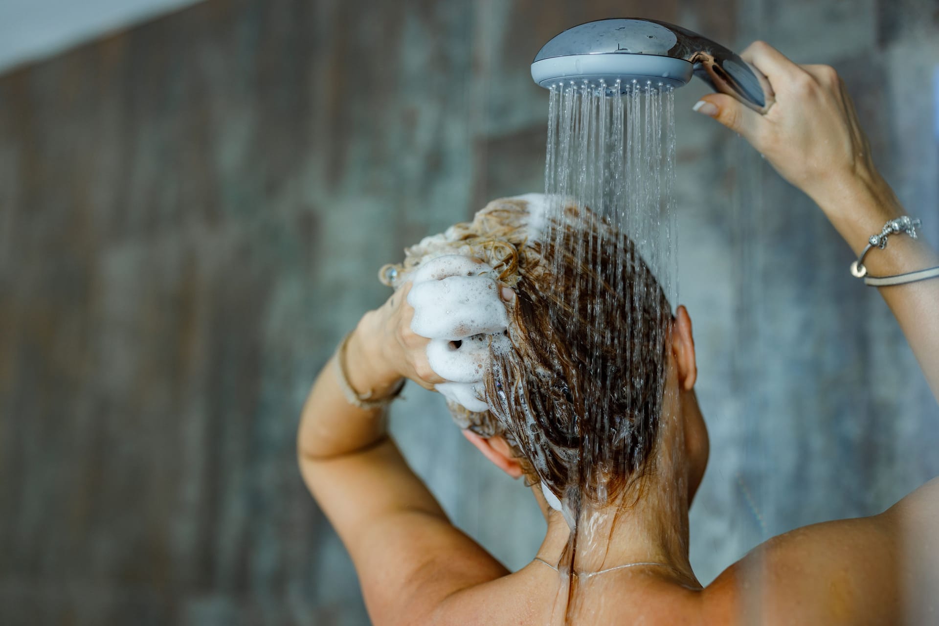 Eine Frau wäscht sich die Haare unter der Dusche.