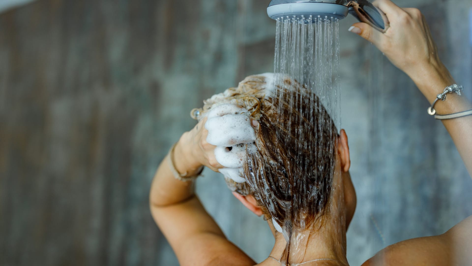 Eine Frau wäscht sich die Haare unter der Dusche.