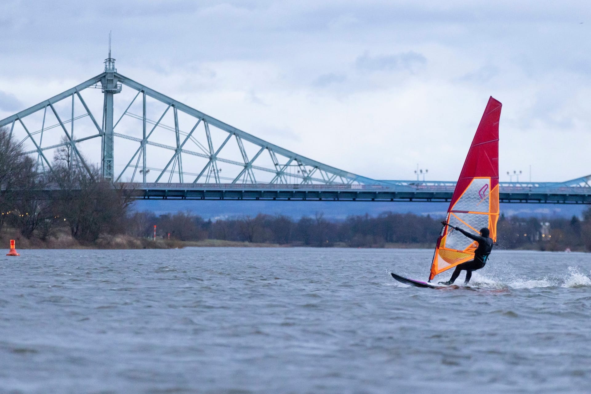 18.02.2023, Deutschland, Sachsen, Dresden, auf dem Foto Blick auf die Elbe Richtung Tolkewitz mit einem Windsurfer im Vordergrund, dahinter das Blaue Wunder