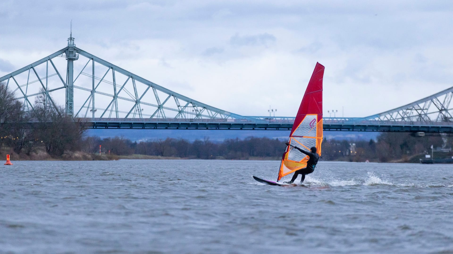 18.02.2023, Deutschland, Sachsen, Dresden, auf dem Foto Blick auf die Elbe Richtung Tolkewitz mit einem Windsurfer im Vordergrund, dahinter das Blaue Wunder