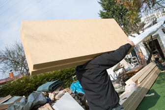 Arbeiter trägt Dämmplatten auf eine Baustelle