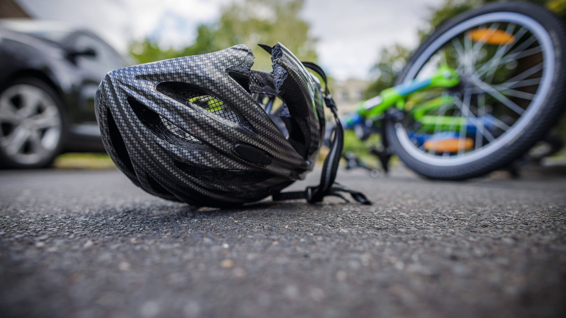 Ein zerbrochener Helm liegt neben einem Fahrrad auf einer Straße (Symbolbild): Ein 17-Jähriger ist an den Folgen eines Unfalls gestorben.