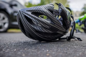 Ein zerbrochener Helm liegt neben einem Fahrrad auf einer Straße (Symbolbild): Ein 17-Jähriger ist an den Folgen eines Unfalls gestorben.