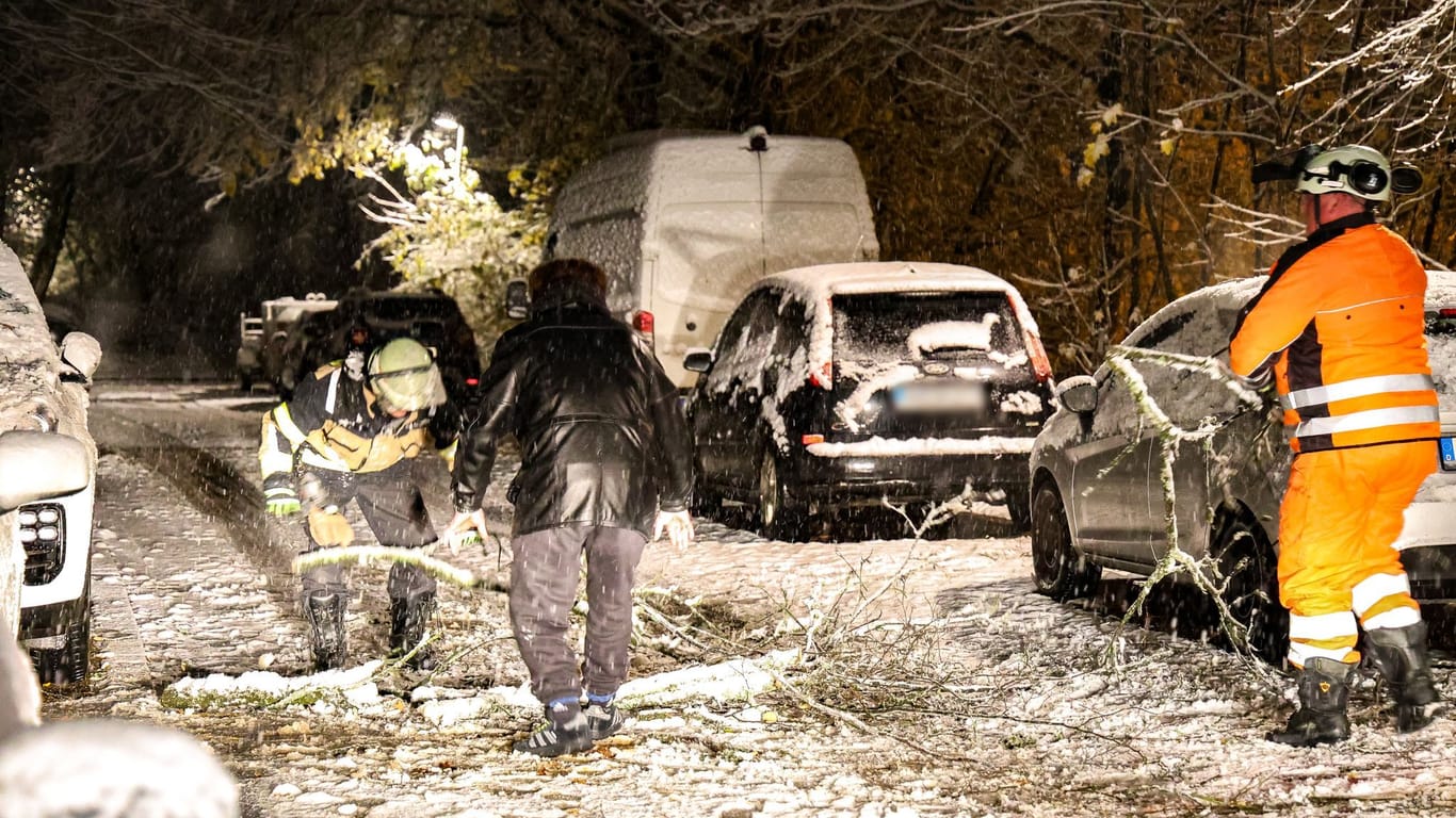 Feuerwehrleute der Berufsfeuerwehr Solingen und ein Anwohner sägen im Schnee bei einem Einsatz.