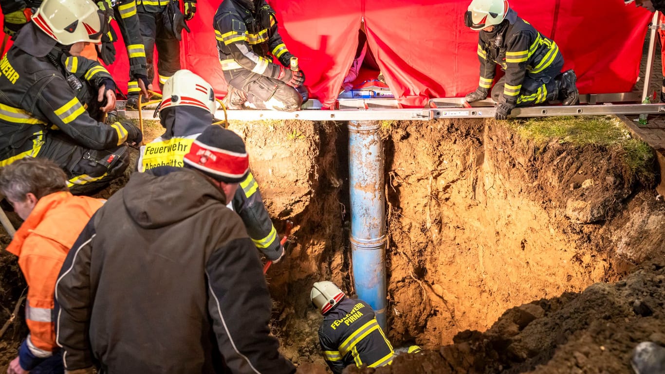 Die Feuerwehr gräbt den Weg frei: Ein kleiner Junge war durch eine Abdeckung auf einer Wiese drei Meter tief in ein Rohr gestürzt.