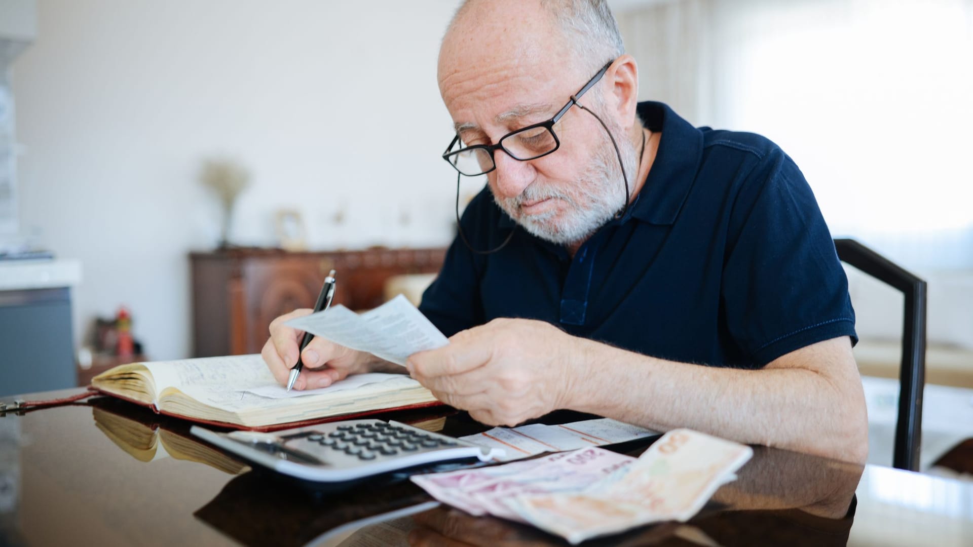 Älterer Mann prüft seine Finanzen: Bei einer Teilrente bezieht man zunächst nur eine reduzierte Altersrente.