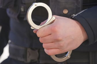 Ein Polizist hält Handschellen in der Hand (Symbolbild): Die Staatsanwaltschaft klagt einen 23-Jährigen wegen versuchten Mordes und Vergewaltigung an.