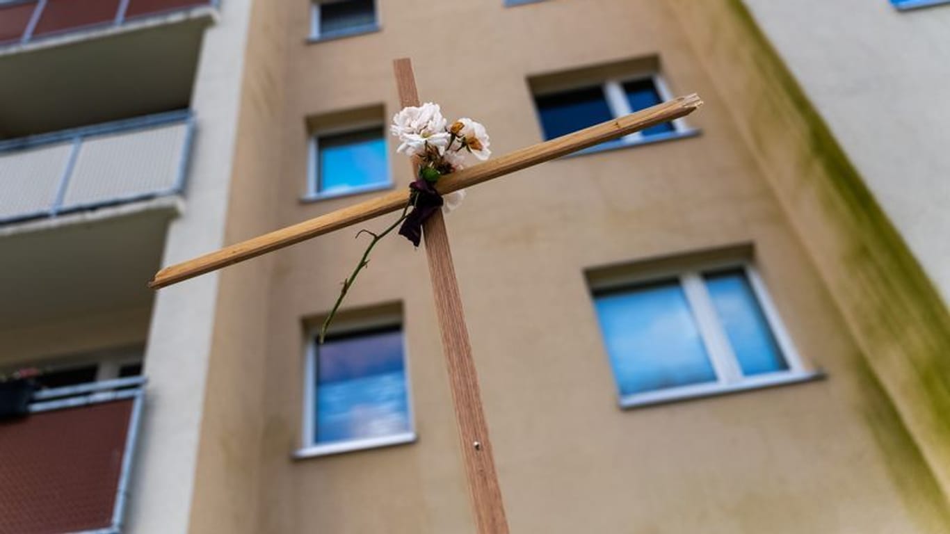 Ein Kreuz mit Blume steht vor einem Rostocker Hochhaus: Ein Mann sprang dort samt Baby auf dem Arm aus dem zehnten Stock.