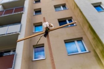 Ein Kreuz mit Blume steht vor einem Rostocker Hochhaus: Ein Mann sprang dort samt Baby auf dem Arm aus dem zehnten Stock.