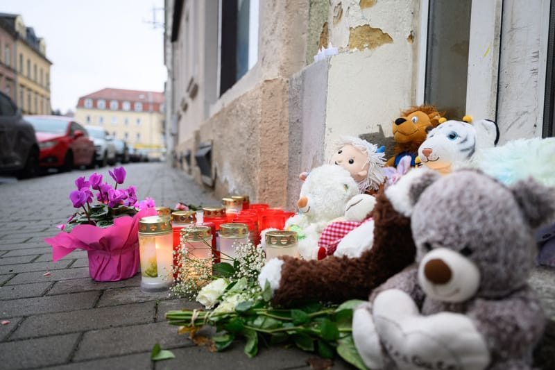 Blumen und Kuscheltiere sind vor einem Haus abgelegt. In einem Mehrfamilienhaus in der Straße sind drei Kleinkinder im Alter von einem, zwei und drei Jahren sowie ein 37-jähriger Mann tot gefunden worden. Die Ermittler gehen von einem Tötungsdelikt aus, wie sie am Montag mitteilten.