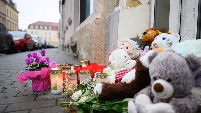 Blumen und Kuscheltiere sind vor einem Haus abgelegt. In einem Mehrfamilienhaus in der Straße sind drei Kleinkinder im Alter von einem, zwei und drei Jahren sowie ein 37-jähriger Mann tot gefunden worden. Die Ermittler gehen von einem Tötungsdelikt aus, wie sie am Montag mitteilten.