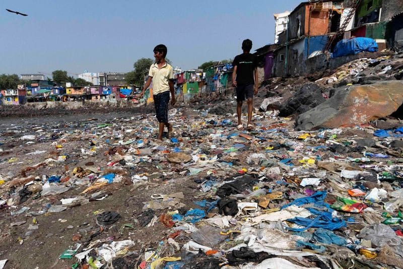 Menschen spazieren am Strand des Badhwar Park an der Küste des Arabischen Meeres an Plastikmüll vorbei. (Archivbild)