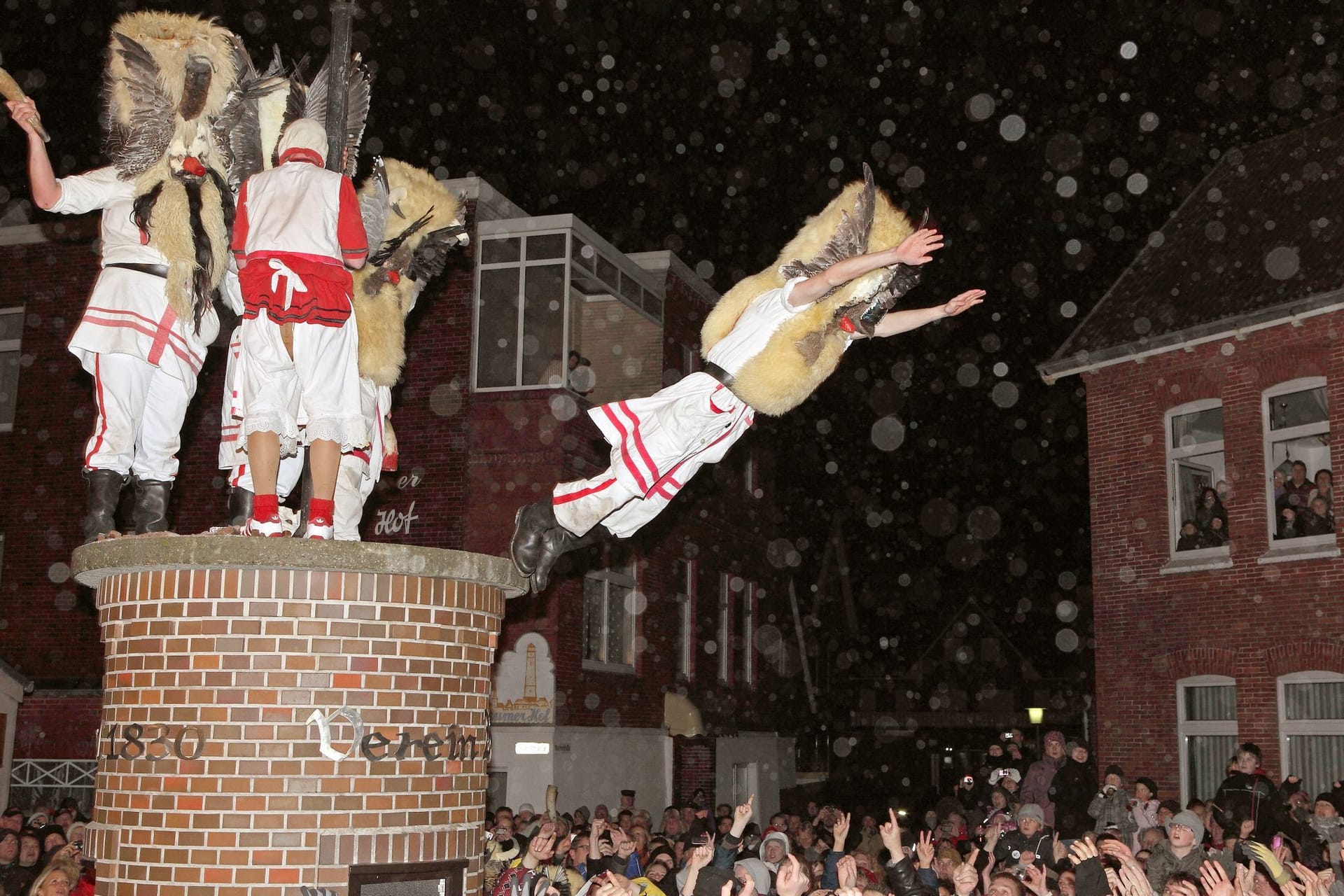 Mit Masken verkleidete Männer des Vereins Borkumer Jungens stürzen sich von einer Litfaßsäule in die Arme der Schaulustigen (Archivfoto).