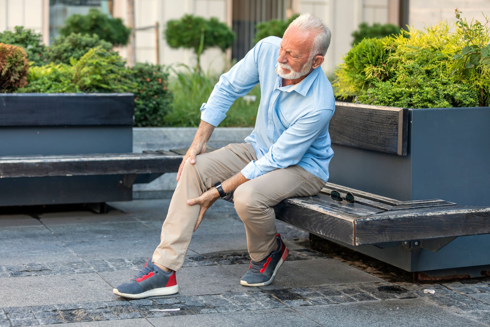 Ein älterer Mann sitzt auf einer Bank und hält sich Knie und Wade.