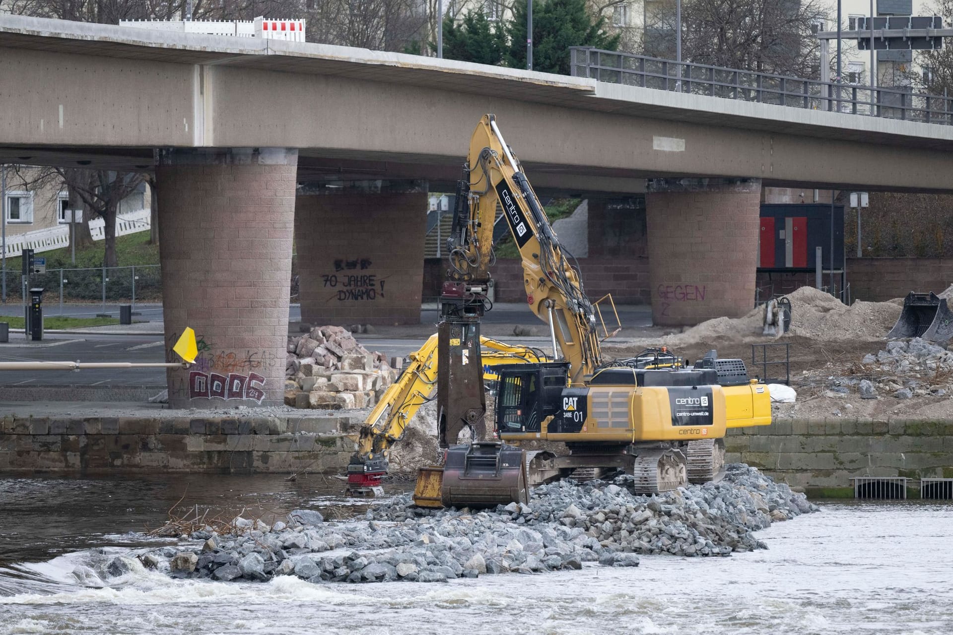 Bagger sind auf der Altstädter Elbseite am eingestürzten Brückenzug der Carolabrücke auf einer Baustraße inmitten der Elbe mit dem Abriss der Brückenteile beschäftigt. Die Abbrucharbeiten werden mit einem sinkenden Elbpegel wieder aufgenommen.