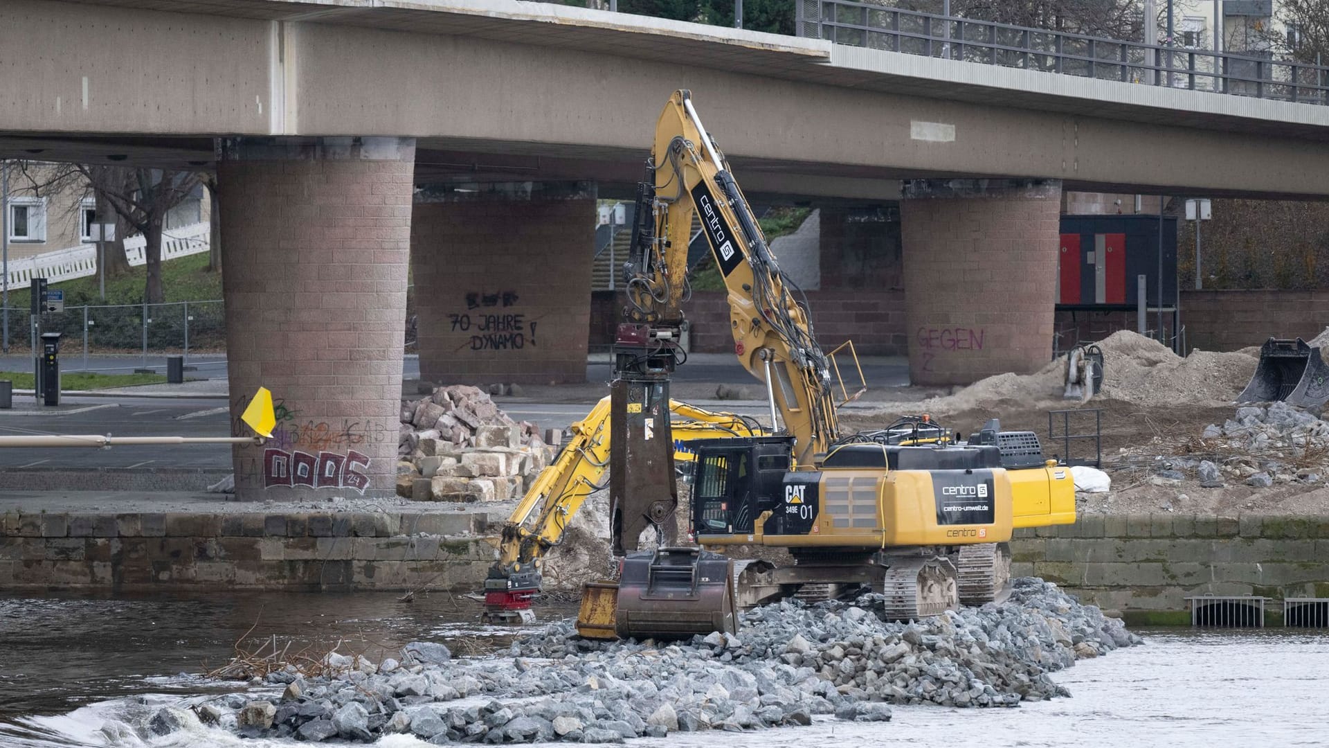 Bagger sind auf der Altstädter Elbseite am eingestürzten Brückenzug der Carolabrücke auf einer Baustraße inmitten der Elbe mit dem Abriss der Brückenteile beschäftigt. Die Abbrucharbeiten werden mit einem sinkenden Elbpegel wieder aufgenommen.