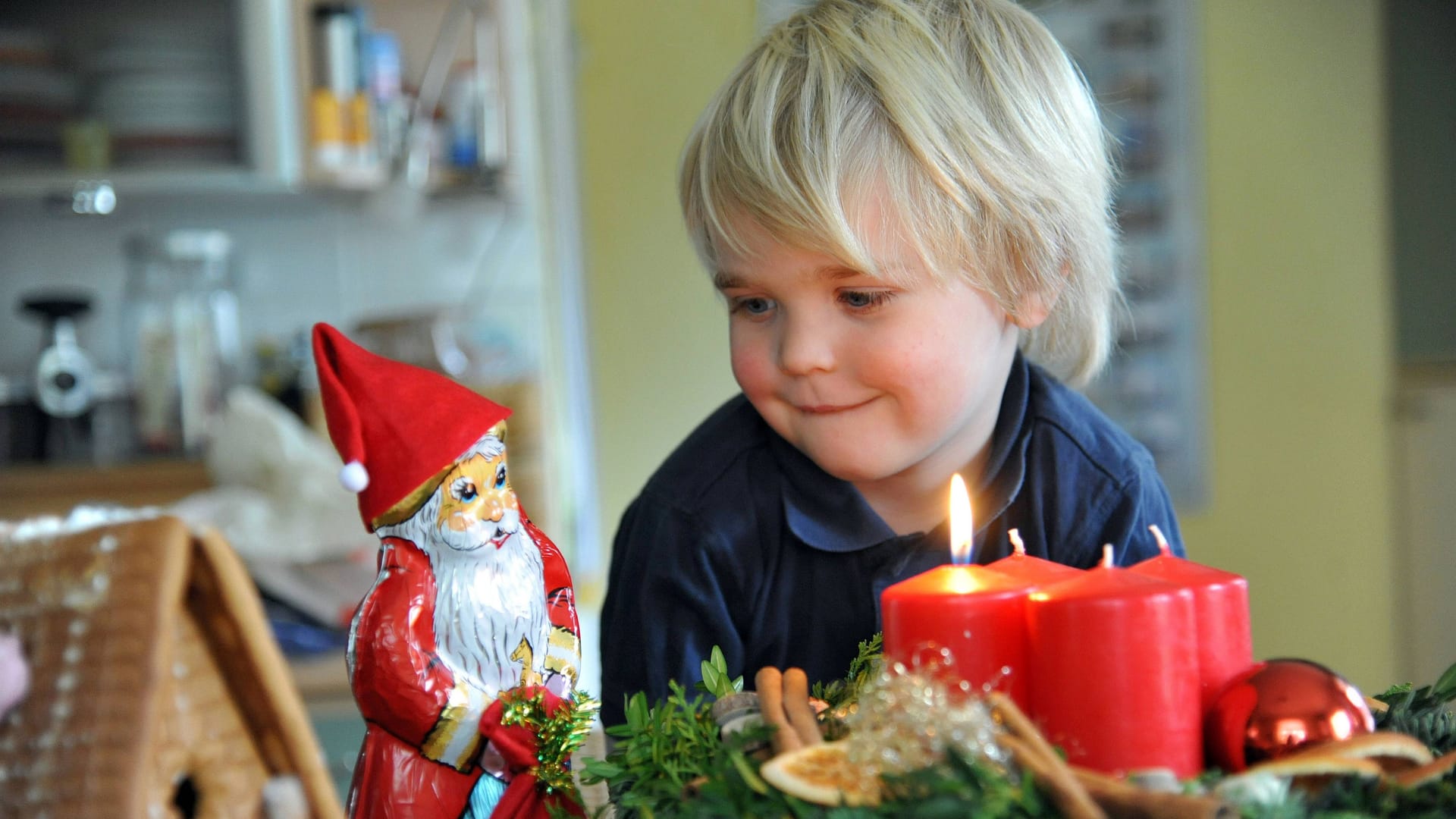 Ein Junge schaut auf einen Adventskranz mit brennender Kerze: Die Idee entstand vor fast zwei Jahrhunderten in Hamburg.