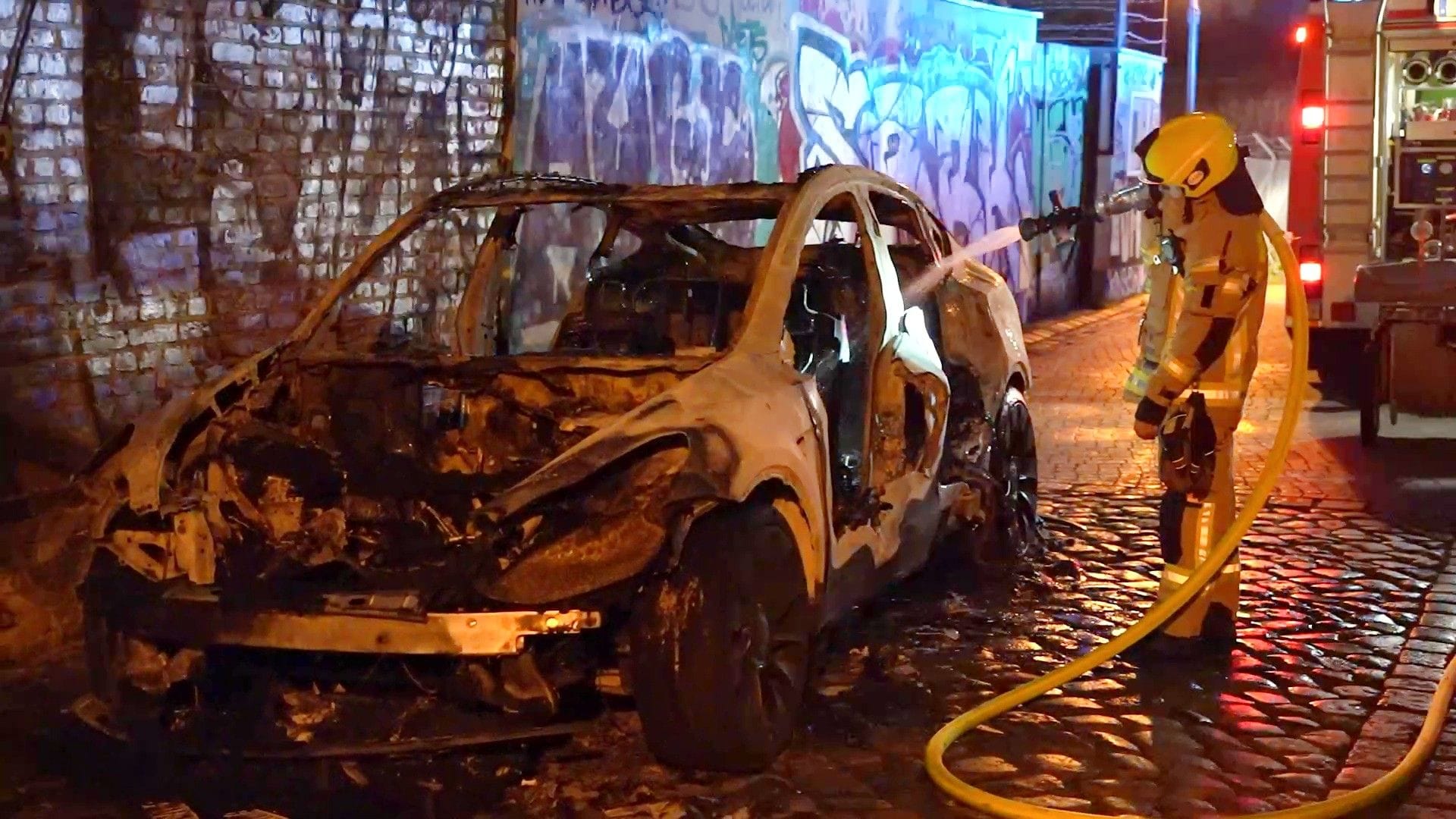 Feuerwehrmann bei einem ausgebrannten Tesla in der Berliner Silvesternacht. (aufgehellt)