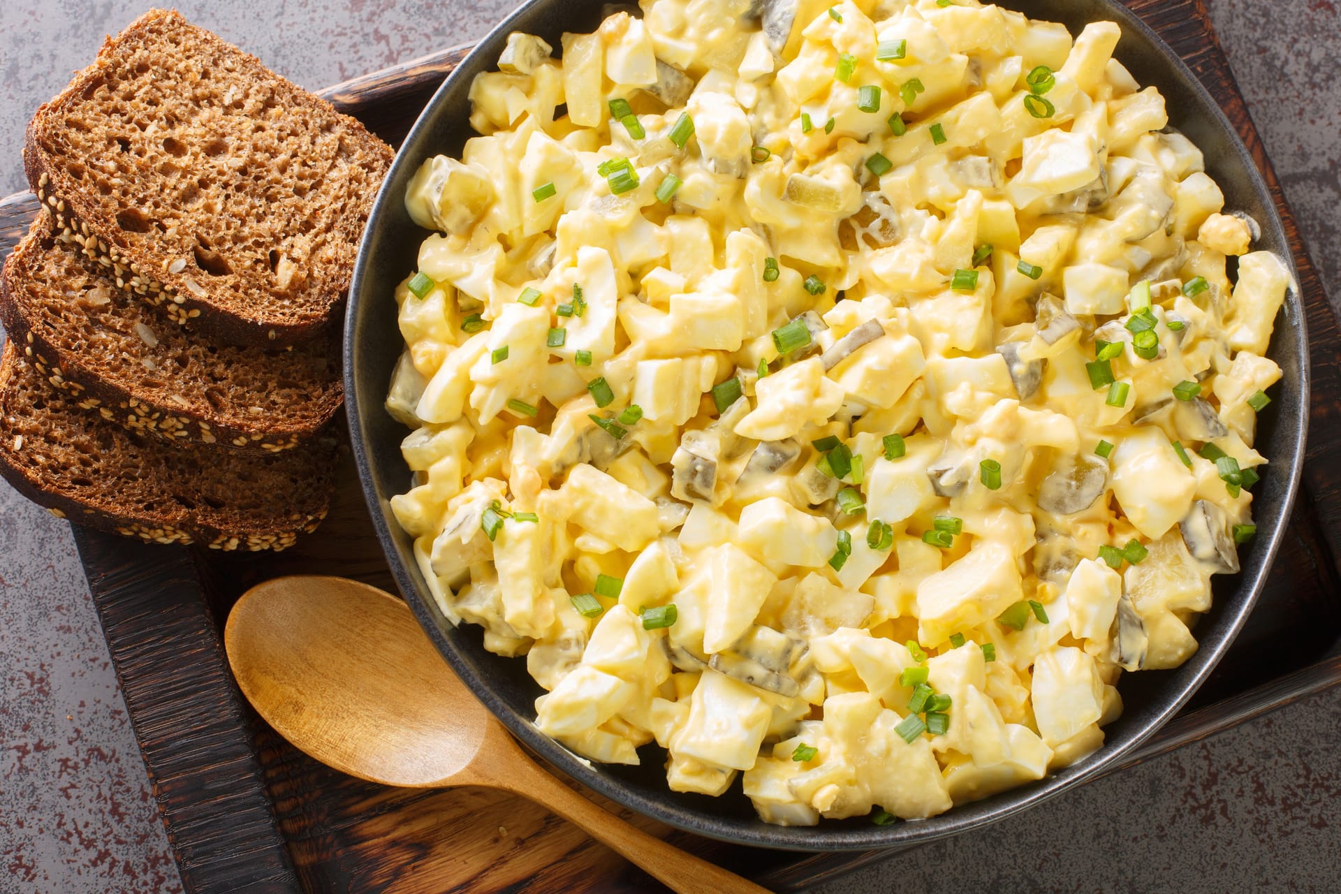 Eiersalat is a creamy German egg salad with cubes of crisp apple and crunchy sour pickles. closeup on the wooden board. Horizontal top view