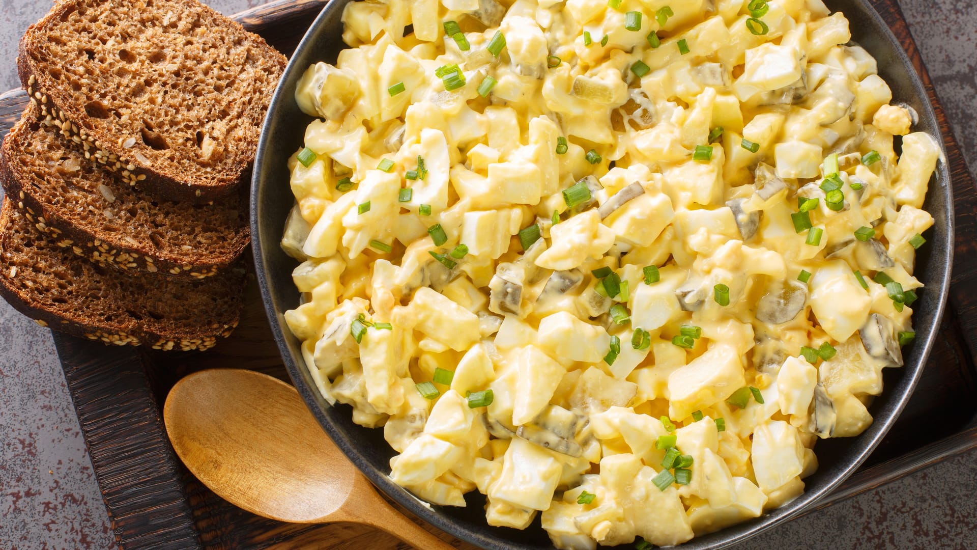 Eiersalat is a creamy German egg salad with cubes of crisp apple and crunchy sour pickles. closeup on the wooden board. Horizontal top view