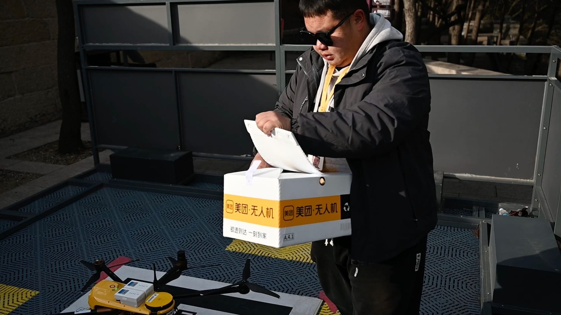 Mitarbeiter des Dienstleisters Meituan am Drohnen-Landeplatz der Großen Mauer bei Badaling, öffnet eine Lieferbox. In China können sich Menschen an immer mehr Orten Essen, Getränke und andere Güter liefern lassen.