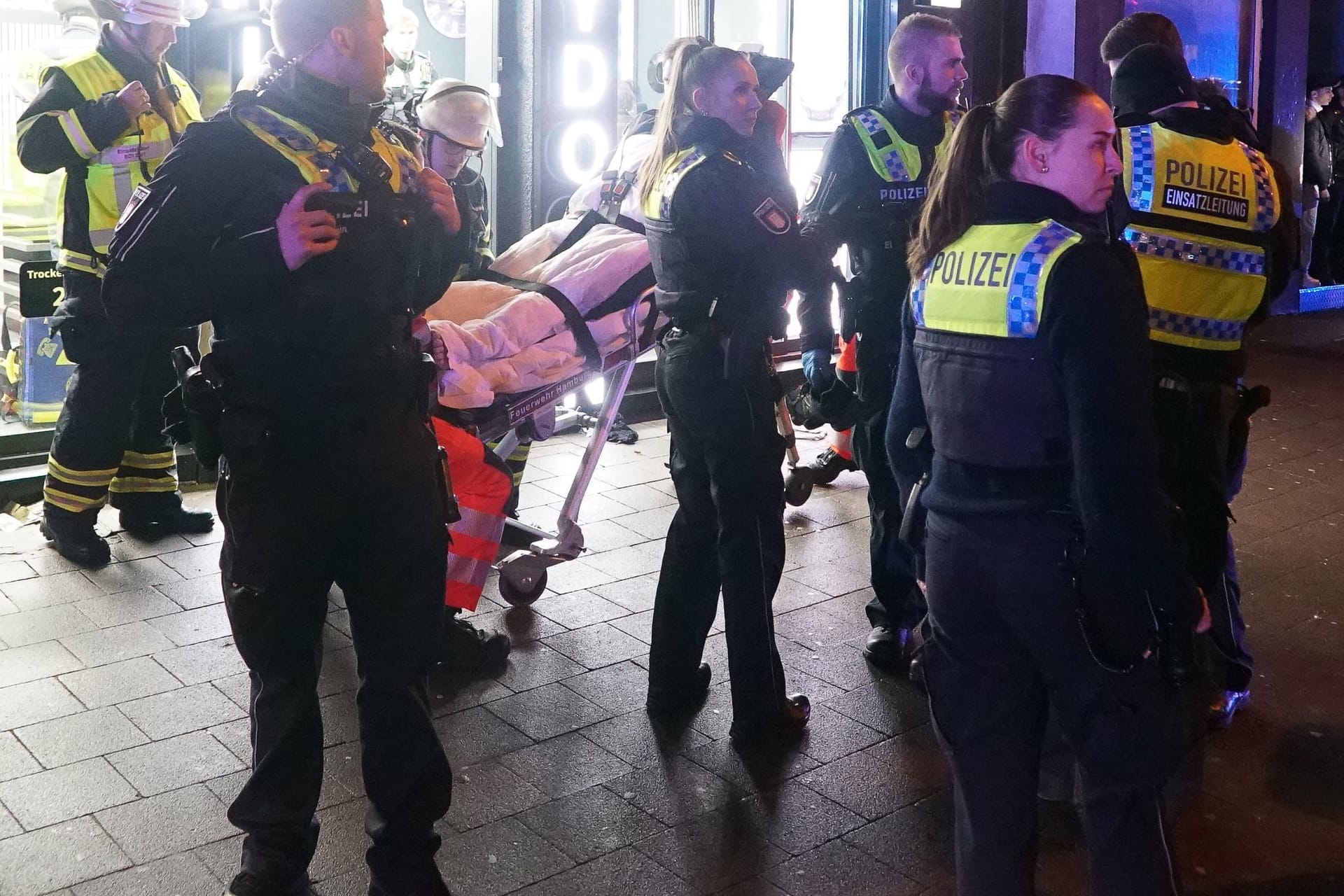 Einsatzkräfte der Polizei stehen neben einem auf einer Trage liegenden Verletzten vor einem Friseursalon in Hamburg-Billstedt.