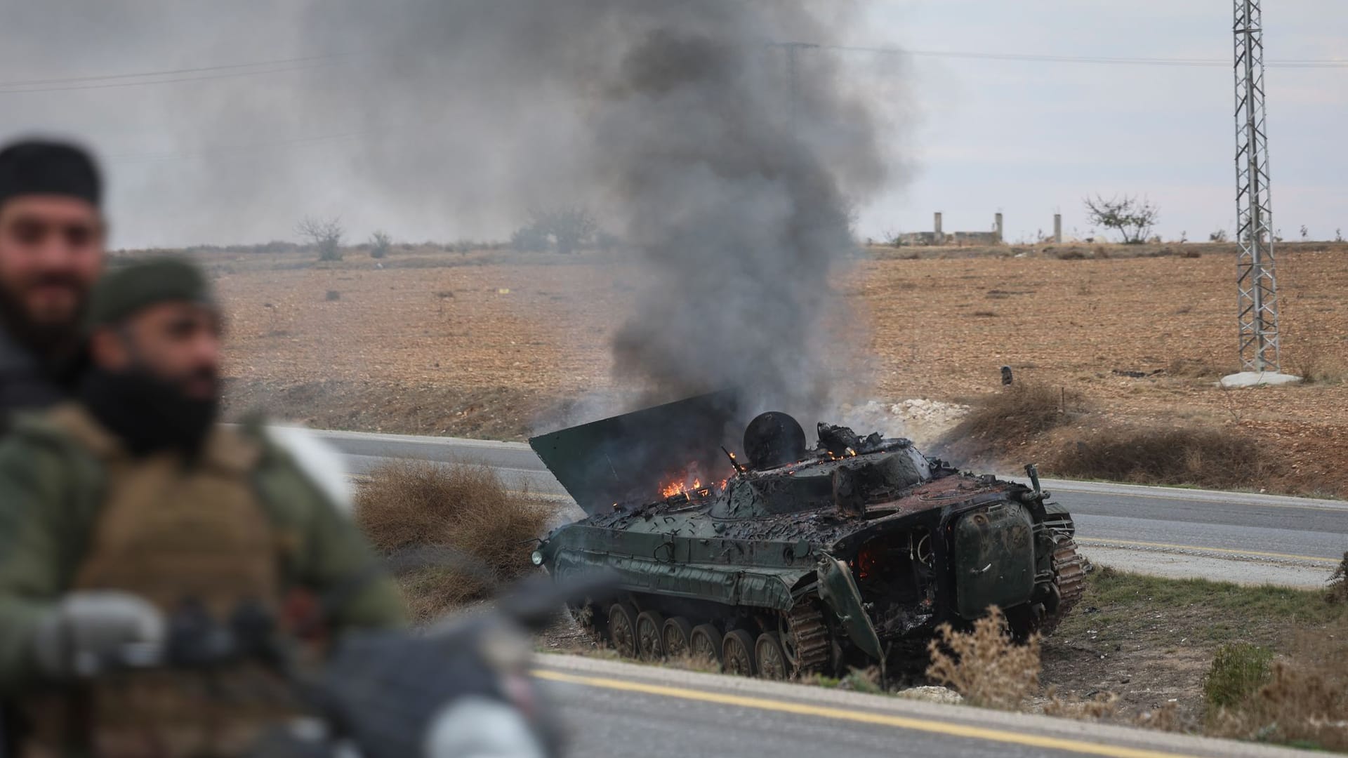 Hama: Syrische Oppositionskämpfer fahren an einem brennenden gepanzerten Fahrzeug der Regierung vorbei.