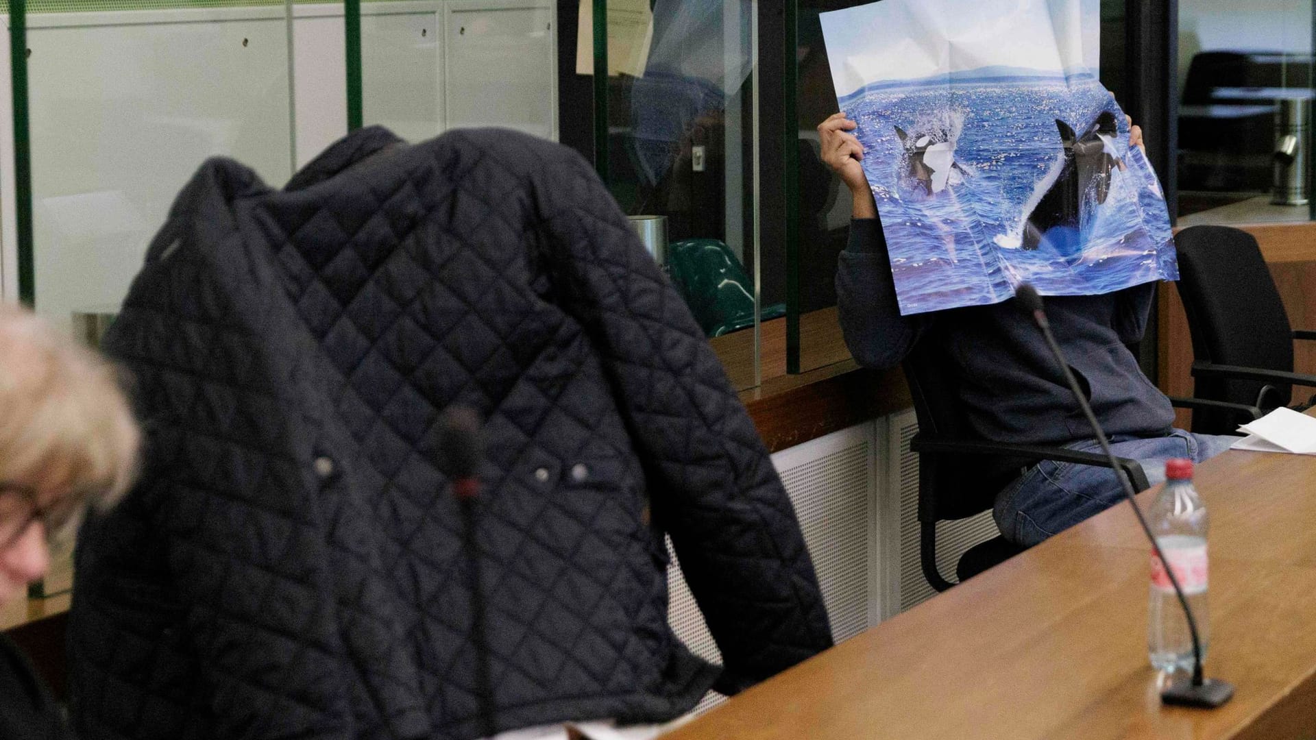 Die beiden Angeklagten (Archivbild): Sie verdecken sich hinter einer Jacke und einem Poster beim Prozessauftakt im Berufungsprozess nach der Serie rechtsextremer Straftaten.