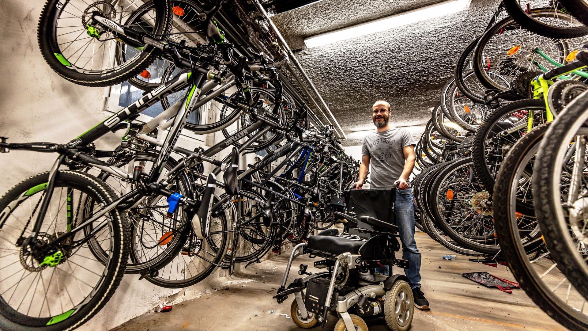 Oliver Laubrock mit einem elektrischen Rollstuhl: Im Fahrradkeller werden unzählige Räder gelagert, die später versteigert werden.