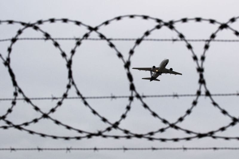 Ein Flugzeug startet - fotografiert durch Stacheldraht am Flughafenzaun.