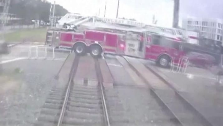 Ein Zug fährt auf einen Bahnübergang zu, auf dem sich ein Feuerwehrauto befindet.