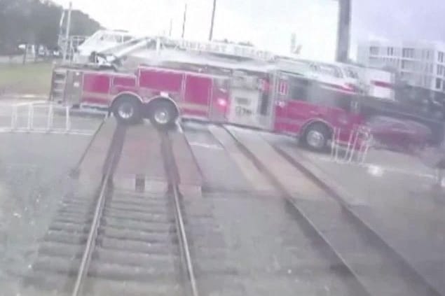 Ein Zug fährt auf einen Bahnübergang zu, auf dem sich ein Feuerwehrauto befindet.