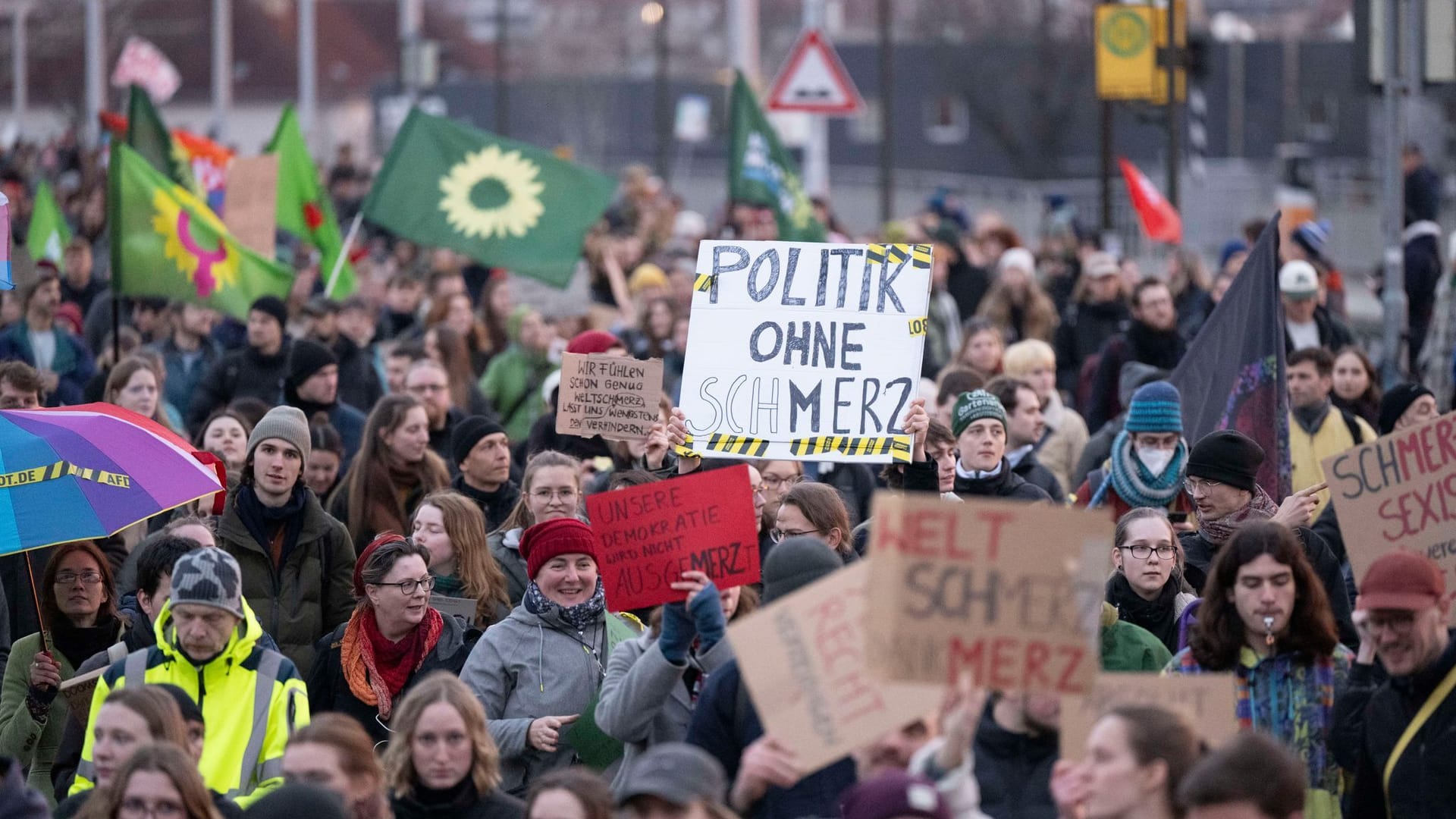 Teilnehmer einer Demonstration gegen die Bundestags-Abstimmung zur Migrationspolitik stehen im Messegelände und halten ein Schild mit der Aufschrift "Politik ohne Schmerz".