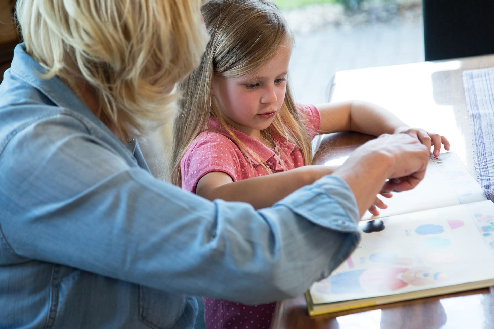 Frau schaut sich mit einem Mädchen ein Kinderbuch an