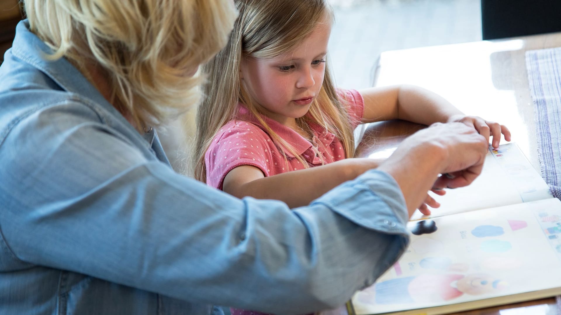 Frau schaut sich mit einem Mädchen ein Kinderbuch an