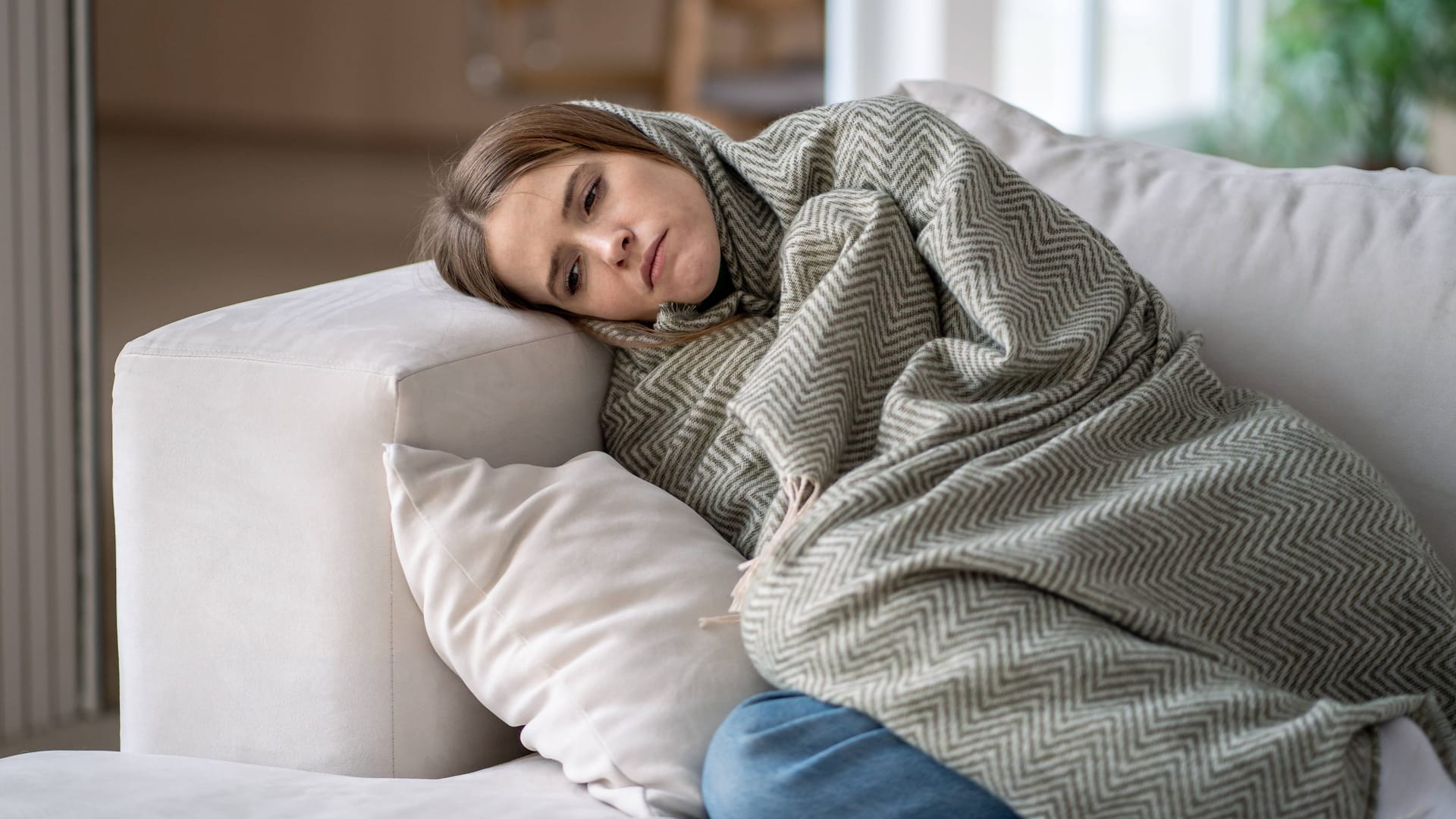 Eine Frau versteckt sich in einer Decke: Im Winter kann die Anfälligkeit für Kopfschmerzen besonders stark sein.