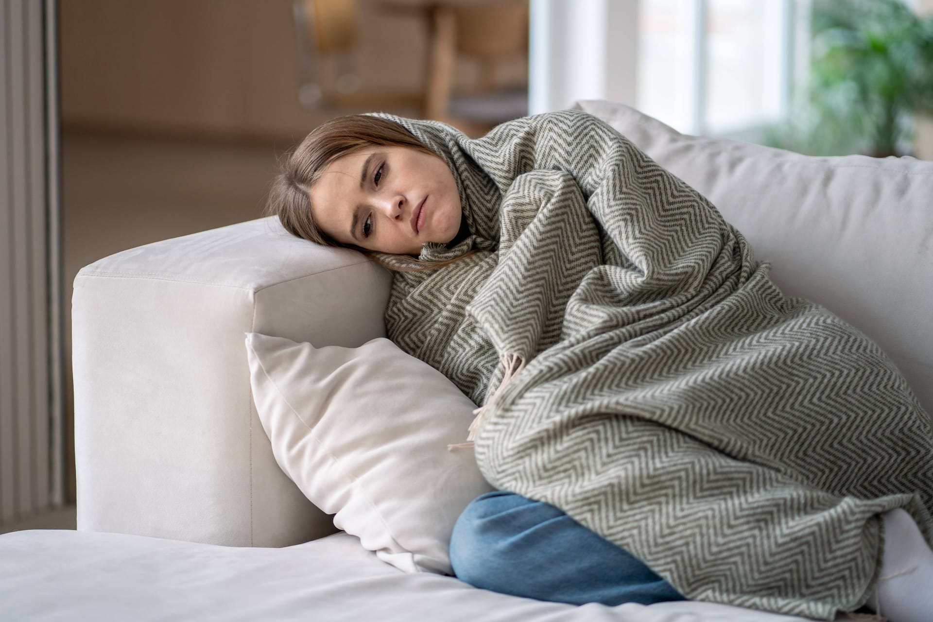 Eine Frau versteckt sich in einer Decke: Im Winter kann die Anfälligkeit für Kopfschmerzen besonders stark sein.