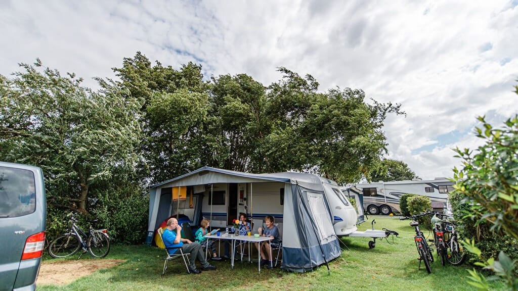 Camping am Deich: Eine Familie hat ihr Zelt windgeschützt hinter Bäumen aufgeschlagen.