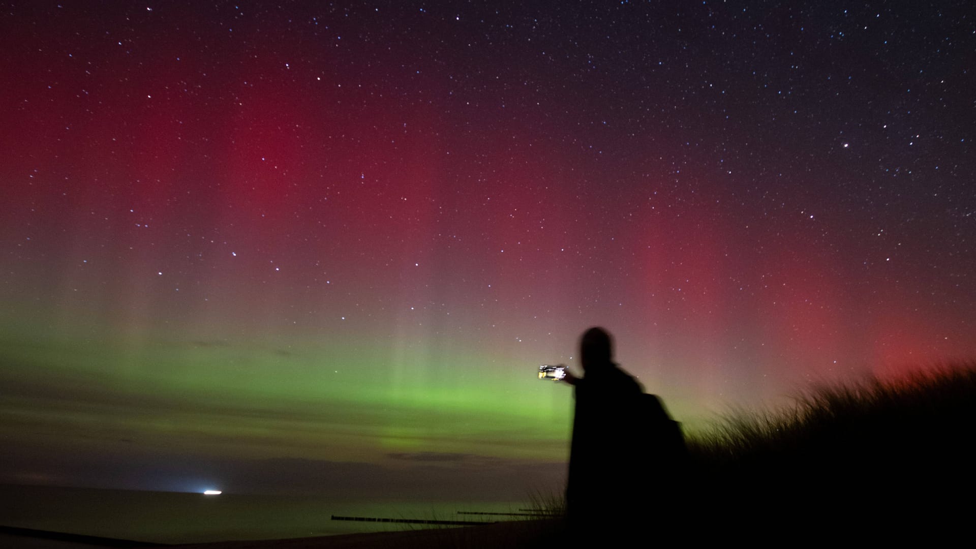 Dierhagen an der Ostsee: Ein Mann beobachtet vom Strand aus Polarlichter und Sternenhimmel.