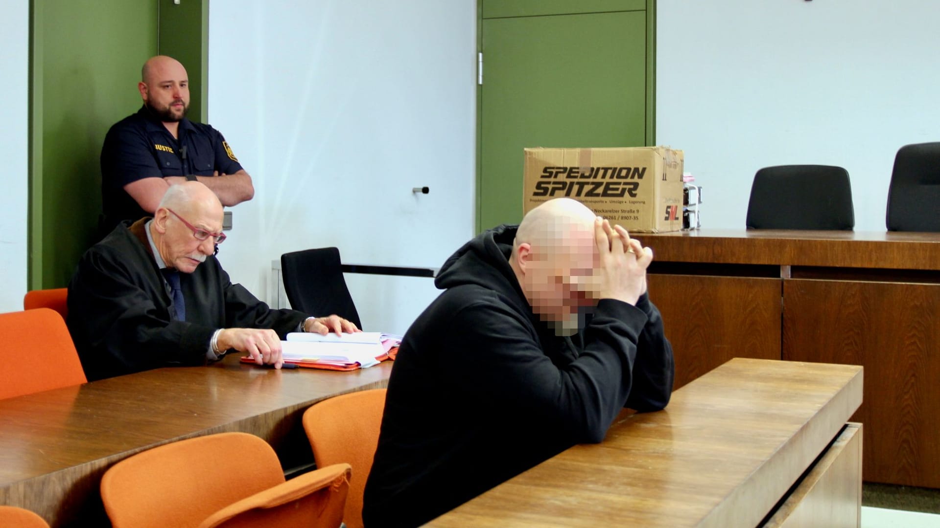 Der Angeklagte im Fall von Schockanrufen in München sitzt vor Gericht, zu Prozessbeginn hat er die Hände vor seinem Gesicht verschränkt.