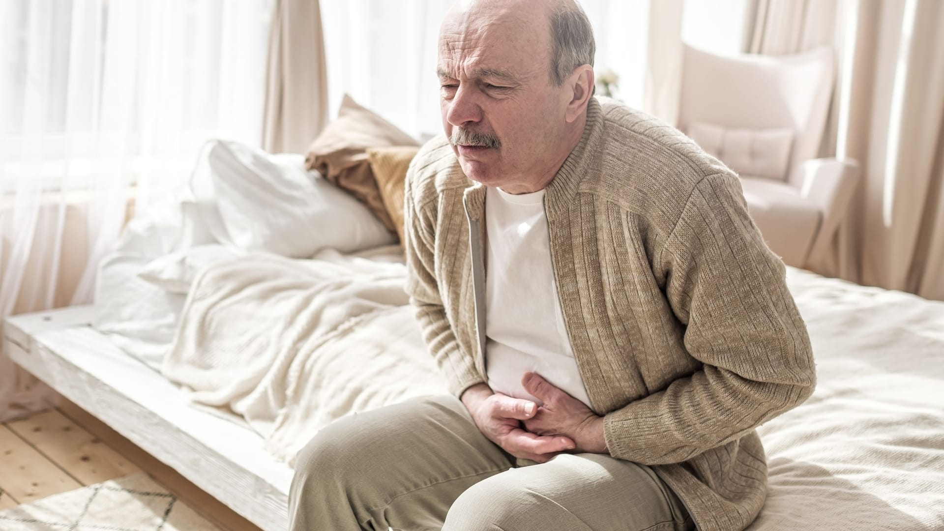 Ein älterer Mann hält sich die Hände vor den Bauch.