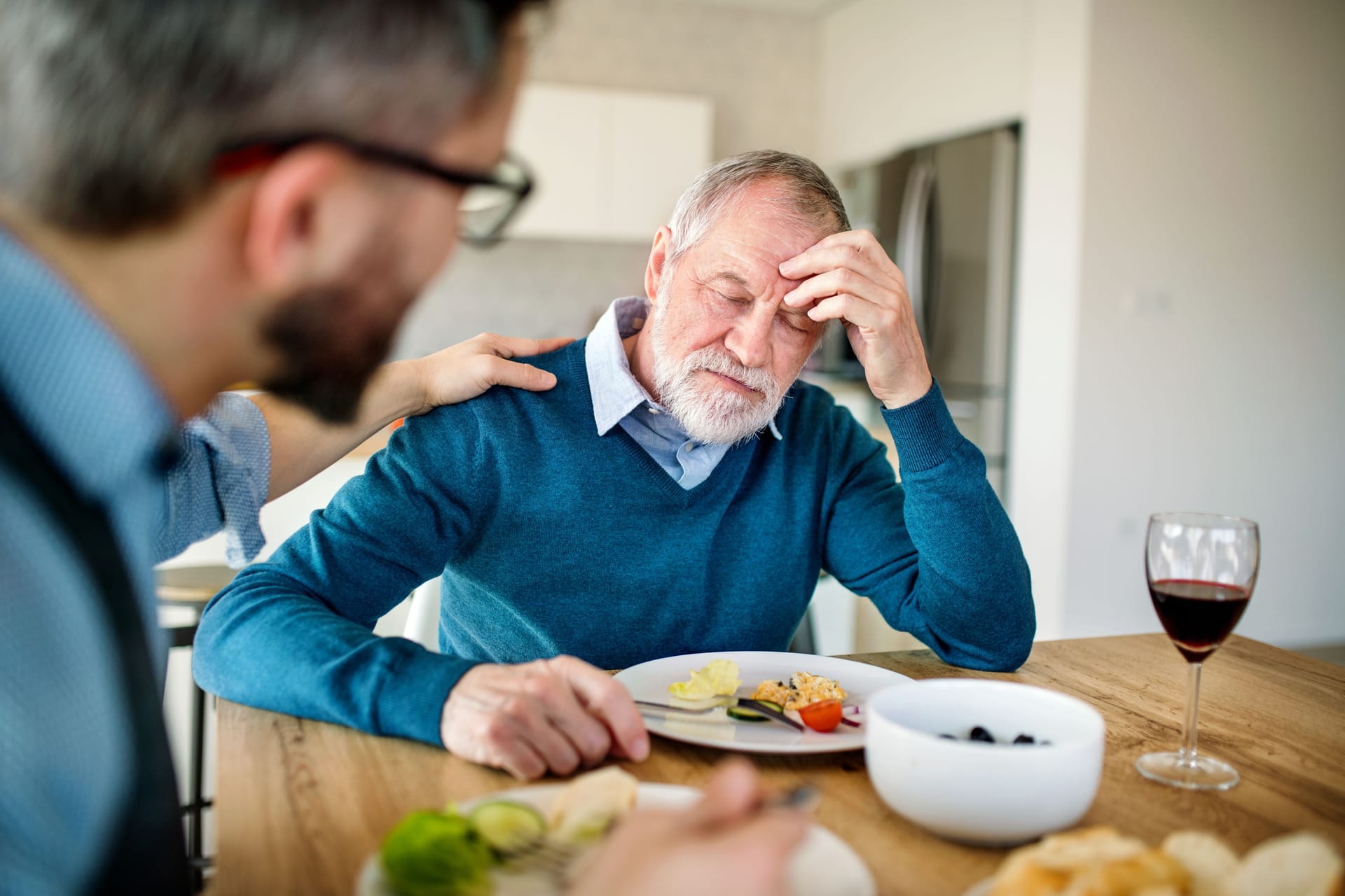 Älterer Mann sitzt am Esstisch und fühlt sich nicht wohl: Tritt Schwindel nach dem Essen auf, kann der Blutdruck eine Ursache sein.