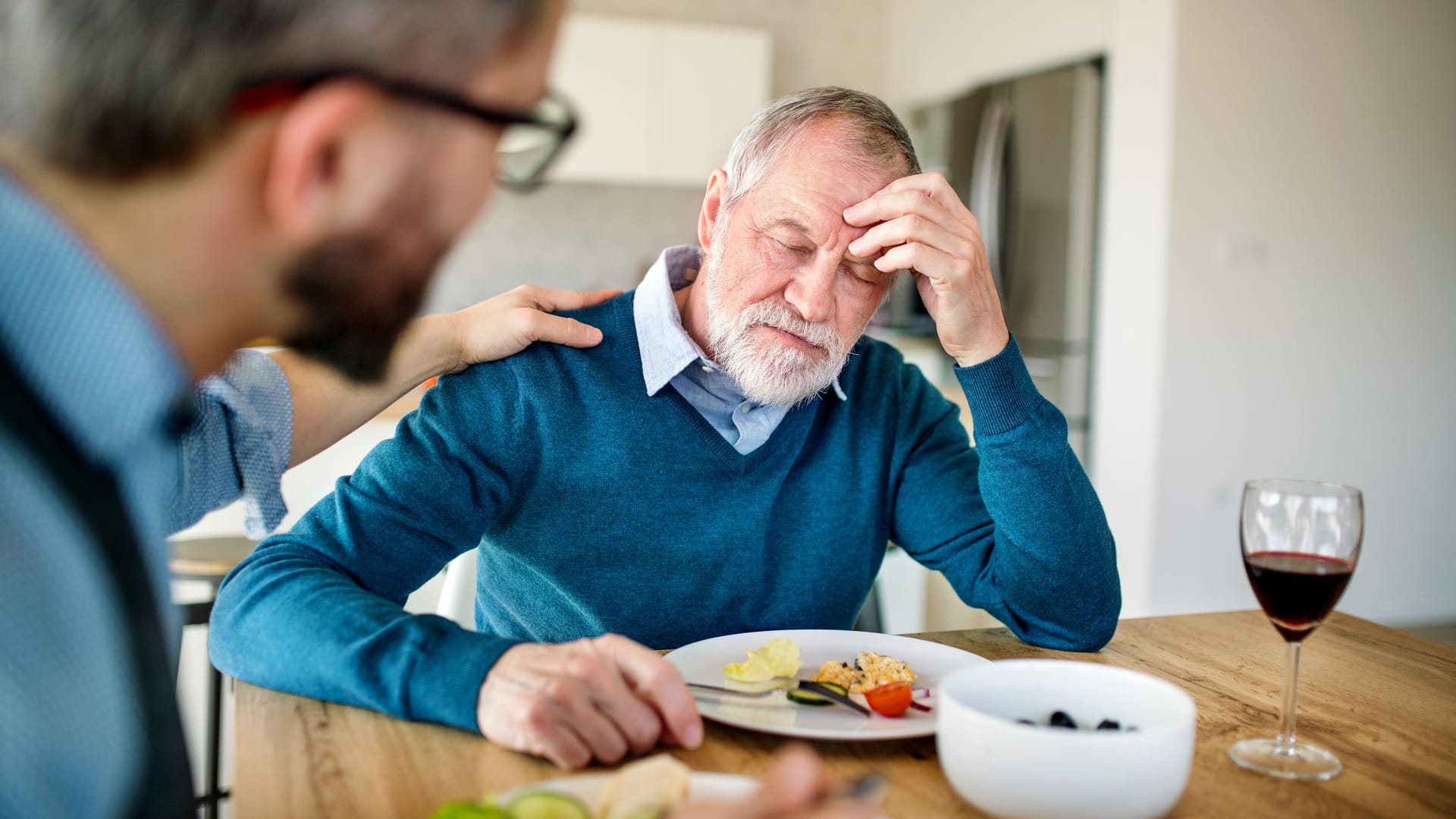 Älterer Mann sitzt am Esstisch und fühlt sich nicht wohl: Tritt Schwindel nach dem Essen auf, kann der Blutdruck eine Ursache sein.