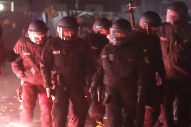 Einsatzkräfte der Polizei stehen in der Silvesternacht zwischen brennendem Feuerwerk in Neukölln.