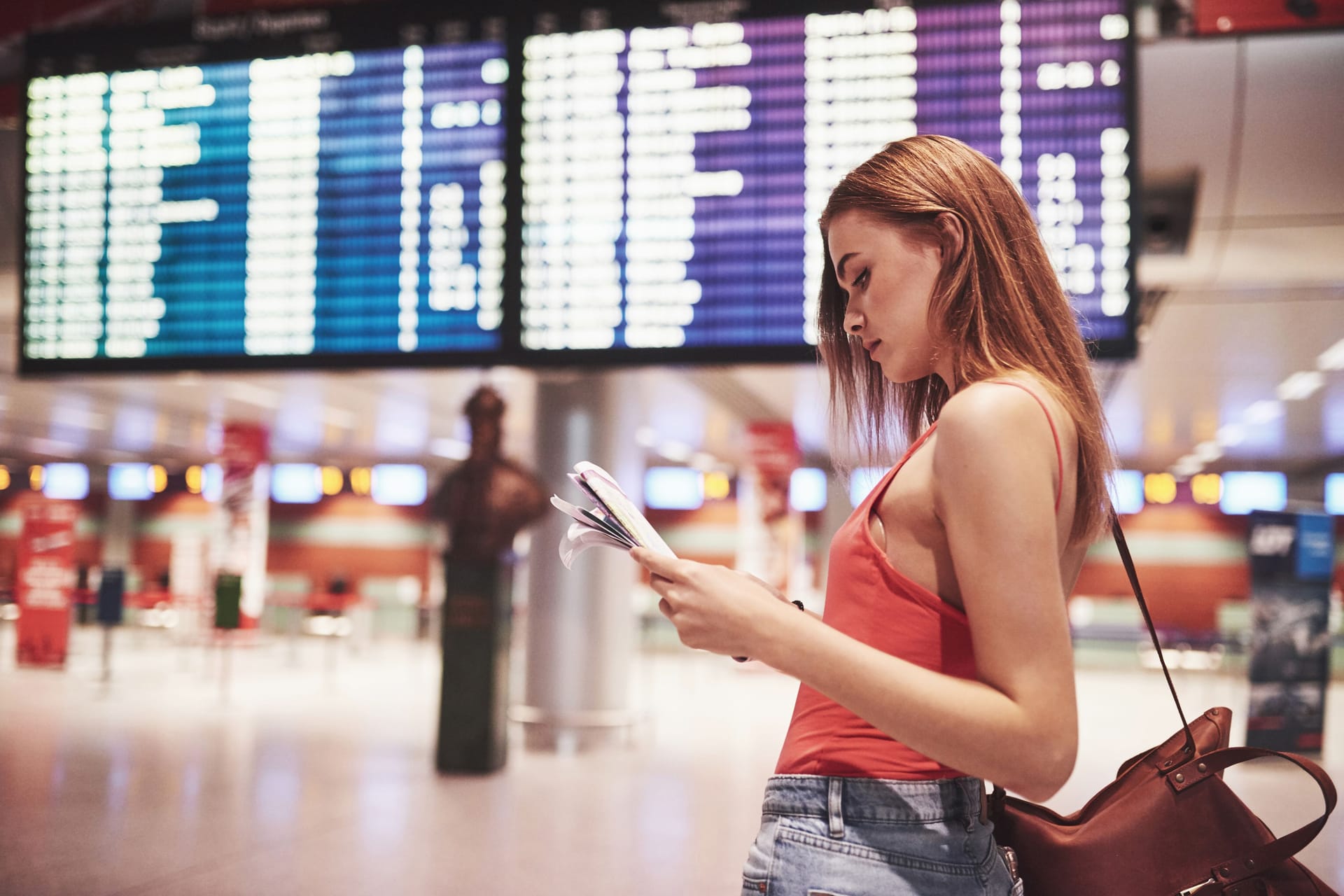 Am Flughafen: Eine junge Frau kontrolliert vor der Anzeigetafel ihren Flugplan.