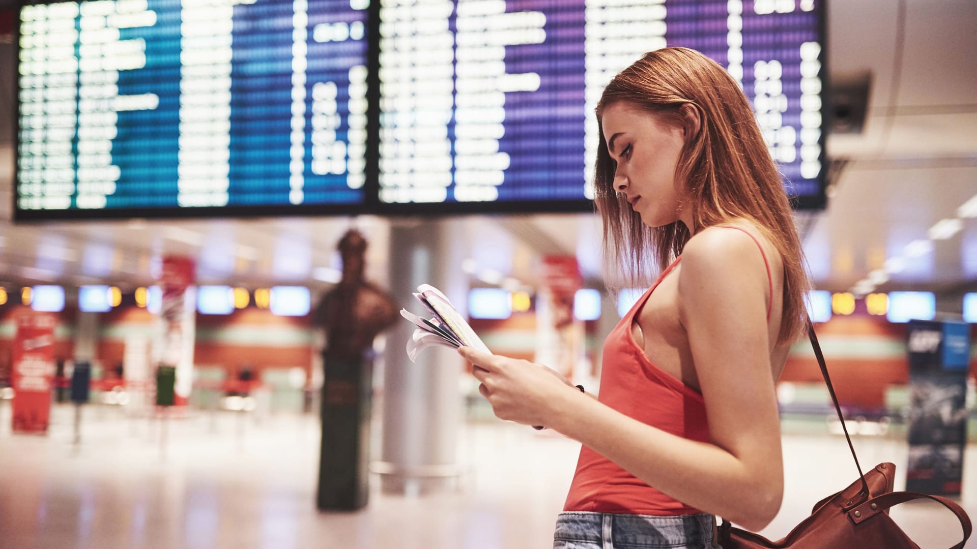 Am Flughafen: Eine junge Frau kontrolliert vor der Anzeigetafel ihren Flugplan.