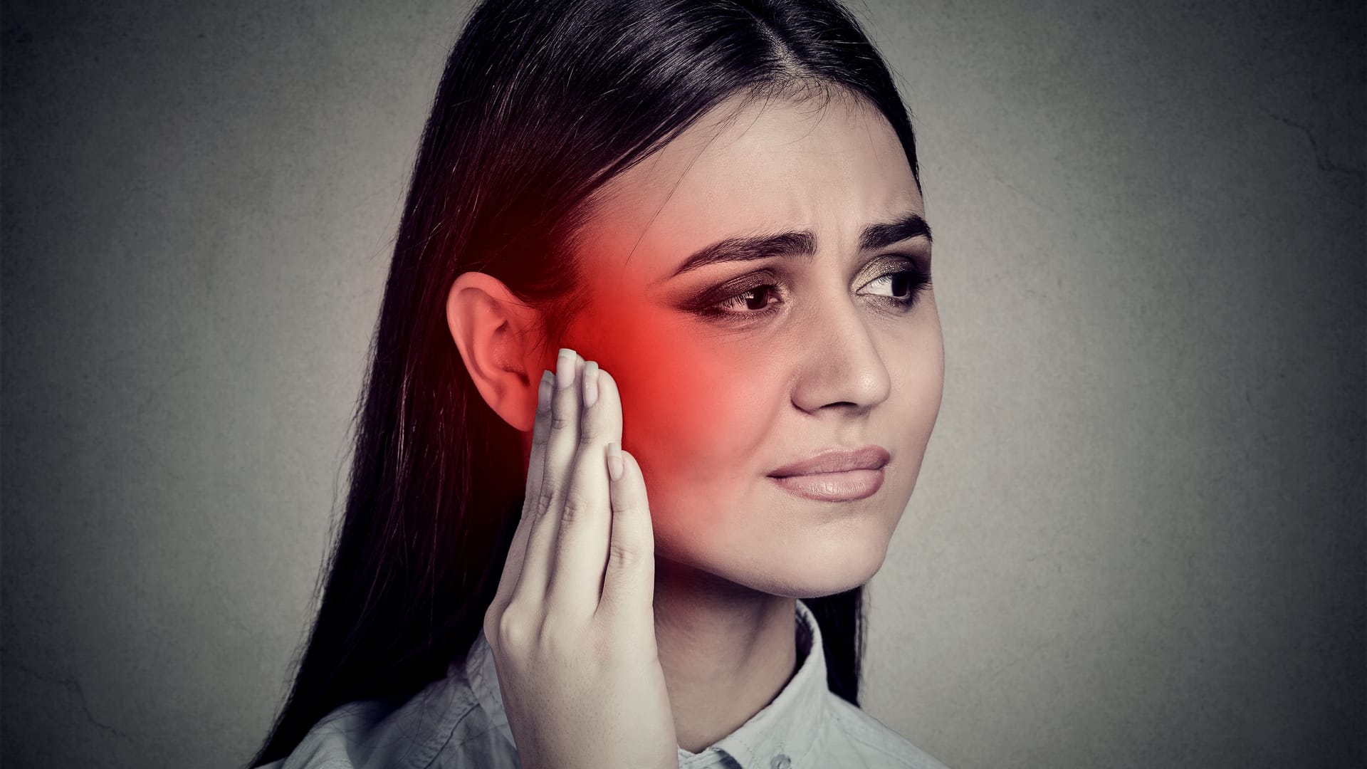 Ursache Tinnitus: Eine junge Frau fasst sich mit schmerzhaftem Gesichtsausdruck an ihr Ohr.