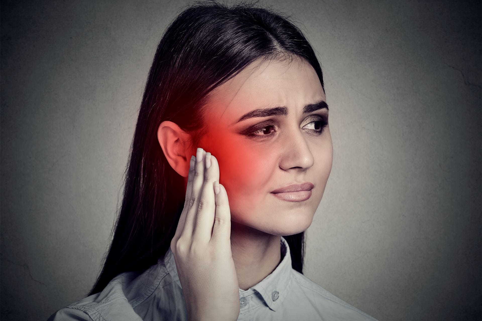 Ursache Tinnitus: Eine junge Frau fasst sich mit schmerzhaftem Gesichtsausdruck an ihr Ohr.