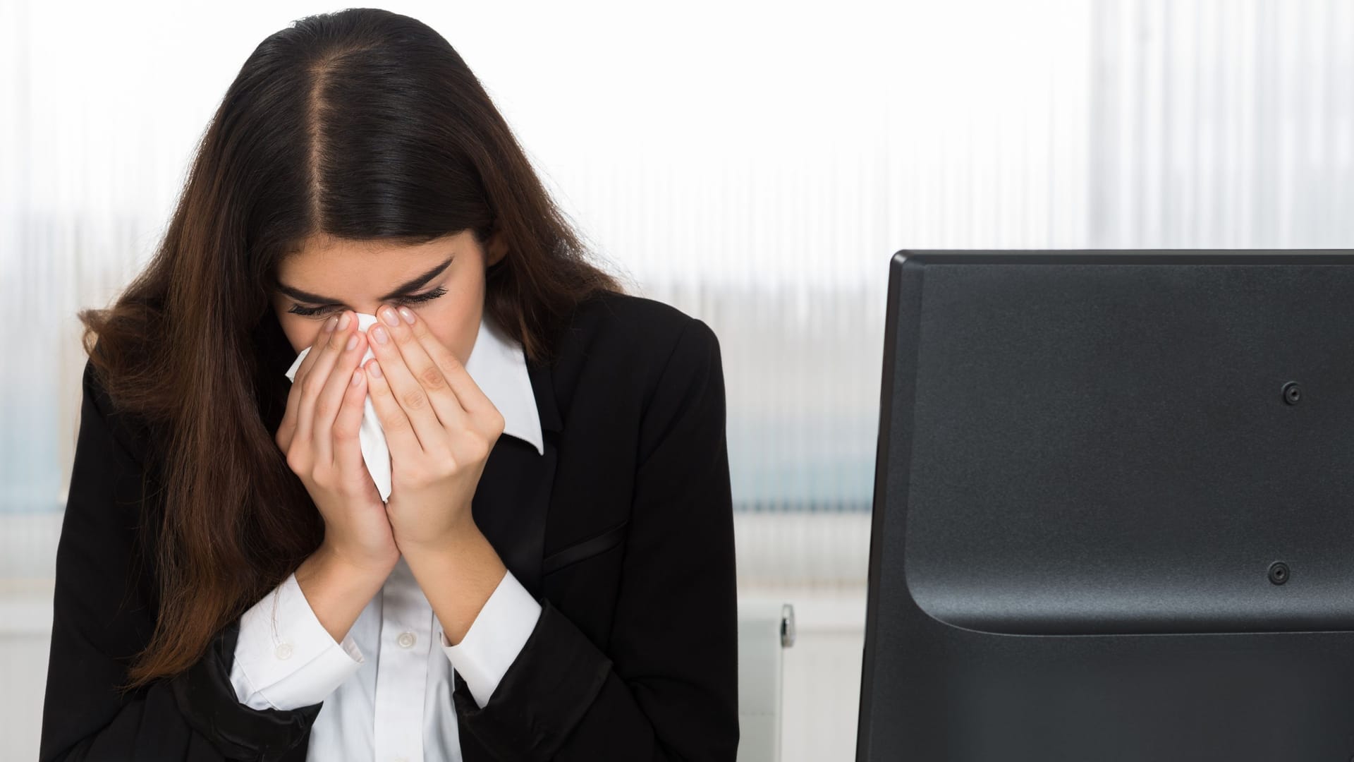 Eine Arbeitnehmerin erscheint krank im Büro (Symbolbild): Karenztage werden kontrovers diskutiert.