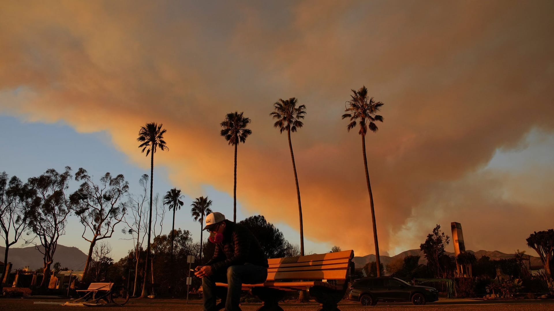 Eine Person sitzt auf einer Bank in Los Angeles, wo noch immer Feuer in den angrenzenden Wäldern wüten.